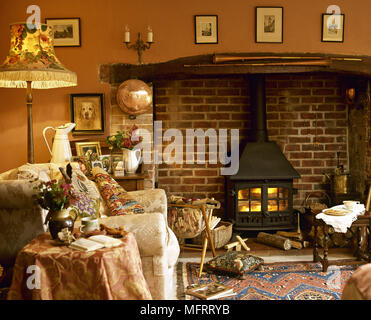 Gemütliches Wohnzimmer mit Kaminecke Holzofen und gepolstertem Sessel. Stockfoto