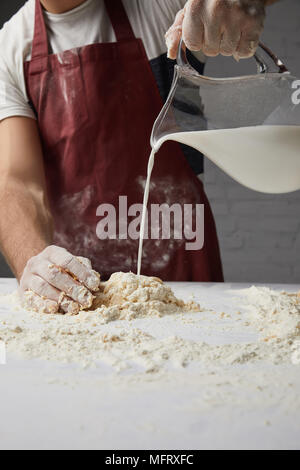 Zugeschnittenes Bild von Chefkoch Zubereitung Teig und Gießen Milch Stockfoto