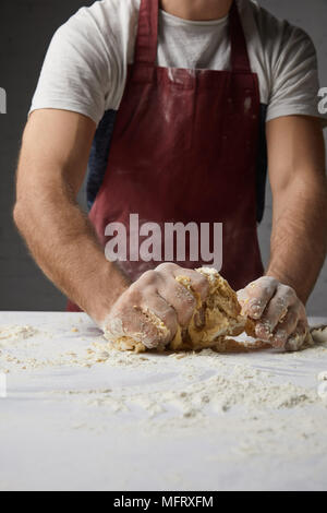 Zugeschnittenes Bild von Chef kneten den Teig auf Tisch Stockfoto