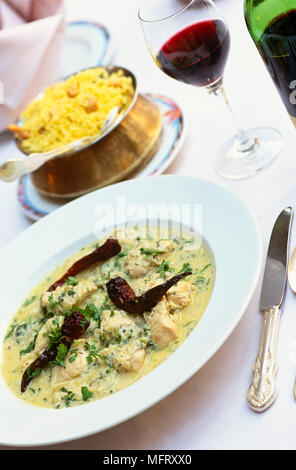 Thai Curry in weißen Porzellanschüssel, Reis Teller und Glas Rotwein Stockfoto