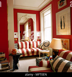 Traditionelle, rote Wohnzimmer mit gestreiften Sofas, Beistelltische, Kunstwerke und einen großen Spiegel. Stockfoto