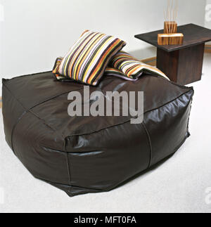 Wohnzimmer mit modernem braunem Leder Bean Bag, gestreiften Kissen und einem Beistelltisch. Stockfoto