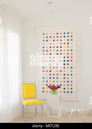 Gerahmte Kunstwerke neben Gelb gepolsterten Stuhl neben Blumen auf der Seite Tabelle Stockfoto