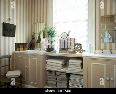 Ein traditionelles, beige Badezimmer mit zwei Waschbecken, in Einheiten gesetzt, gestreifte Tapete, Handtücher, Stockfoto