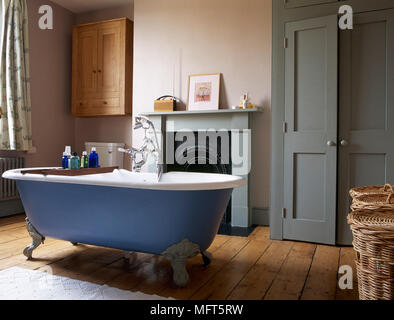 Freistehende Badewanne im Badezimmer mit grün lackierten Schranktüren und Kamin und Holzboden. Stockfoto
