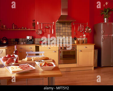 Ein modernes, Küche im Landhausstil mit roten Wänden, gelb Einheiten, Holzböden, Holz Tisch, essen, Mittagessen, Edelstahl Kühlschrank, Stockfoto