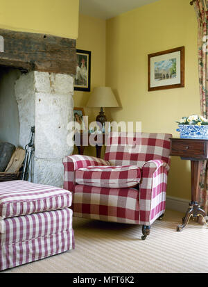 Landhaus Wohnzimmer Detail mit einem karierten Sessel und Ottomane neben einer Kaminecke. Stockfoto