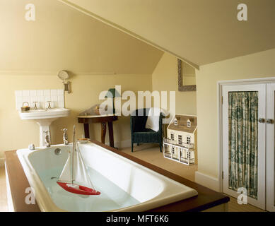 Land gelb Bad mit einer Dachschräge, Badewanne in einem Wald umgeben, Standwaschbecken und Einbauschrank. Stockfoto