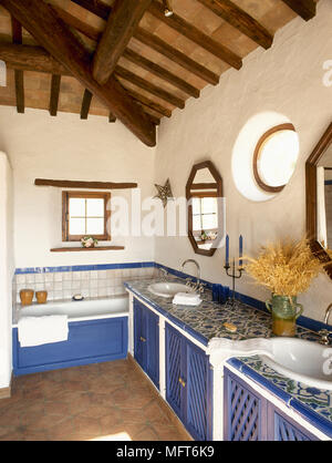 Badezimmer im mediterranen Stil mit Holzbalkendecken, warf die Decke, Doppelwaschbecken in Mosaik Fliesen Waschtisch, Badewanne und geometrischen Fenster und Spiegel. Stockfoto