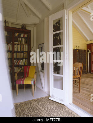 Ein Detail eines Landes Schlafzimmer Bücherregal und Stuhl Fliesenboden und Holzdecken. Französische Türen, die zu Veranda Stockfoto