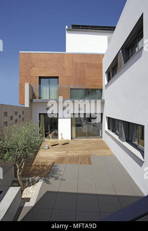 Einzelnen Baum wachsen in der minimalistischen Innenhof mit Holzterrasse und befestigten Flächen Stockfoto