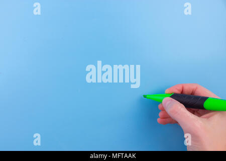 Einer Frau mit einem grünen Stift mit der rechten Hand und Schreiben auf blauem Hintergrund. Stockfoto