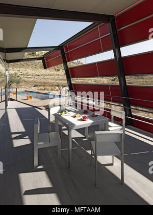 Tisch und Stühle auf der überdachten Terrasse des modernen Haus mit Schwimmbad in der Entfernung Stockfoto