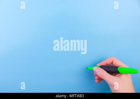 Einer Frau mit einem grünen Stift mit der rechten Hand und Schreiben auf blauem Hintergrund. Stockfoto