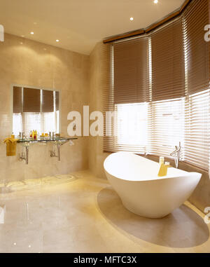 Modernes gefliestes Bad mit skulpturalen freistehende Badewanne, zwei Waschbecken in einem schwimmenden Glas-schminktisch, und sonnigen Fenster mit Jalousien. Stockfoto