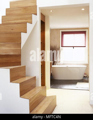 Moderne Flur mit Holztreppen und ein Blick auf ein offenes Badezimmer mit freistehender Badewanne. Stockfoto