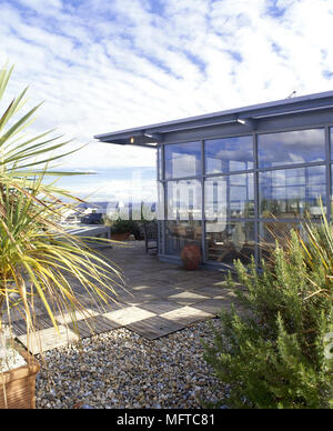 Von außen ein modernes Haus mit Glaswänden, geflieste Terrasse, und Topfpflanzen. Stockfoto