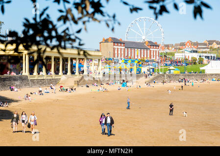 Leute genießen Sie einen Spaziergang am Strand und in der Sonne zu sitzen, an einem warmen Frühlingstag auf Barry Island, Wales Stockfoto