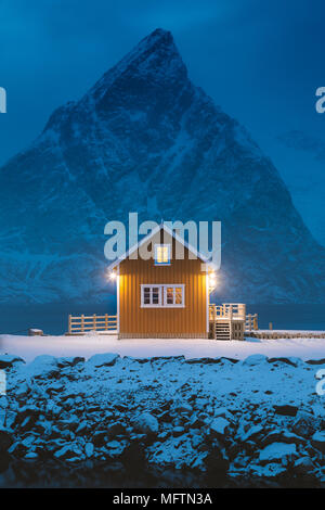 Traditionelle gelb Rorbu Kabine mit Olstinden Mountain Peak in der Dämmerung im Winter Dorf Sakrisoy, Lofoten Inseln, Norwegen Stockfoto