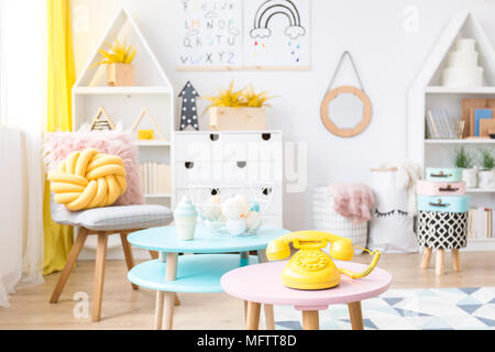 Gelbe Telefon auf Pastell rosa Hocker in kluge Kinder zimmer einrichtung mit Spielzeug und ein kleiner Spiegel an der Wand platziert Stockfoto