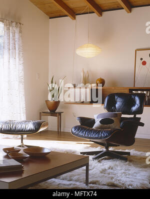 Wohnzimmer Detail mit Retro Leder Charles Eames Stuhl und Hocker Schaffell Teppich Kaffeetisch und gebeizt Holzböden Stockfoto