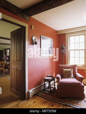 Die Ecke eines traditionellen Wohnzimmer mit roten Wänden und Holzfußboden mit einem roten Sessel neben dem Fenster. Stockfoto