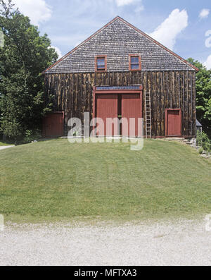 Das Äußere eines traditionellen Scheune mit dunkler Holztäfelung roten Türen und Fenster Stills und eine Leiter an der vorderen Wand lehnt. Stockfoto