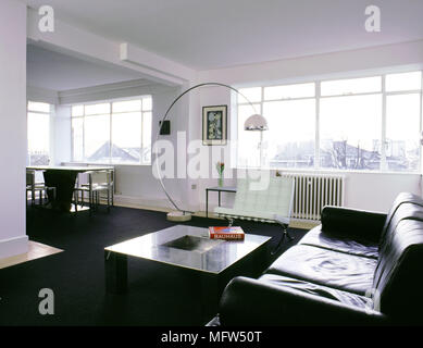 Moderner, offener Wohnbereich mit schwarzer Teppich Esstisch und Stühle leder Sofa geschwungene Stehleuchte und sonnigen Fenster. Stockfoto