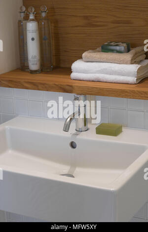 Seife auf einem modernen Waschbecken unter einem Holzregal mit gefalteten Handtücher und Toilettenartikel. Stockfoto