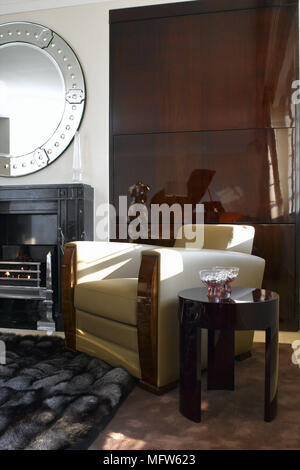 Details eines modernen Sessel mit gelbem Polster mit einem Fell Teppich neben einem kreisförmigen Spiegel über einen Kamin. Stockfoto