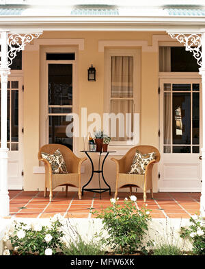 Von außen ein Bungalow mit Korbstühlen auf einer überdachten Veranda. Stockfoto