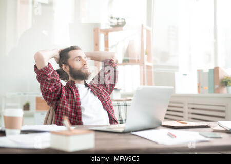 Casual bärtiger Mann an seinem Arbeitsplatz sitzen und denken über etwas Stockfoto