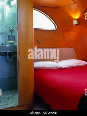 Gemütliches Bett mit roter Abdeckung neben Bad im Pod wie Zimmer mit Bad Stockfoto