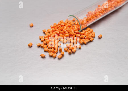 Paletten aus Kunststoff. Farbstoff für Polymere in Granulatform vor. Orange Granulat von Rohstoffen aus Kunststoff für die Industrie verschüttete aus dem Rohr Stockfoto