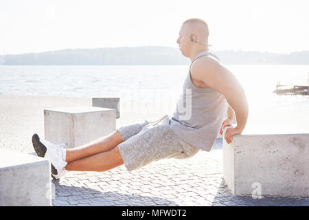 Profil anzeigen von einem starken Mann seine Arme trainieren und dabei tricep Dips im Freien in einer Parkbank Stockfoto