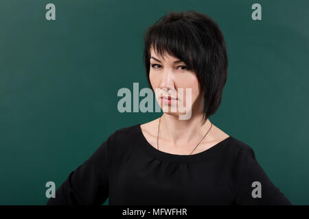 Strenge Mädchen Lehrer durch Chalk Board posiert, Lernkonzept, grüner Hintergrund, Studio shot Stockfoto