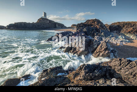 Wellen auf felsigen Strand mit alten lighhouse auf Felsen im Hintergrund. Ynys LLanddwyn im Nordwesten Anglessey, Wales, Großbritannien Stockfoto