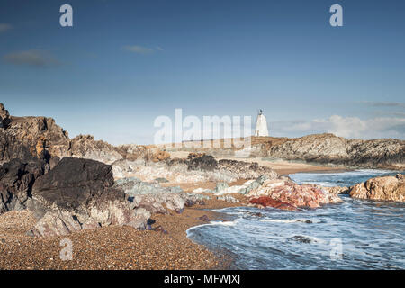 Küsten Szene von Wellen auf dramatische felsigen Ufer mit alten weißen lighouse im Hintergrund. Llandwyn Insel im Nordwesten Anglessey, Wales, Großbritannien Stockfoto