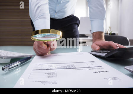 Nahaufnahme der Kaufmann Hand mit Lupe über Rechnung am Arbeitsplatz Stockfoto