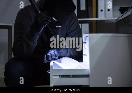 Dieb Holding Taschenlampe stehlen Dokument aus Schublade im Büro Stockfoto