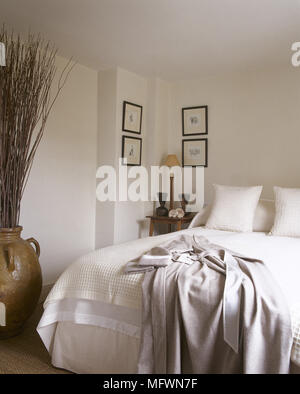 Twig Anordnung in der Keramik Urne neben Doppelbett in neutralen Farben Schlafzimmer Stockfoto