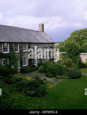 Außenansicht einer rustikalen Landhaus aus Stein mit einem üppigen, grünen Rasen und Sträucher. Stockfoto