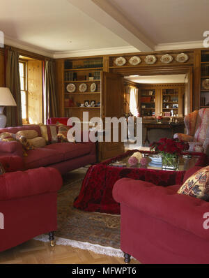 Wohnzimmer mit roten Sofas und Stühlen, Couchtisch mit Stoffbezug in Zimmer mit holzgetäfelten Wänden Stockfoto