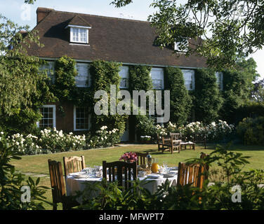 Tabelle mit Einstellungen im Garten des Landhauses in Laub und Rasen bedeckt Stockfoto