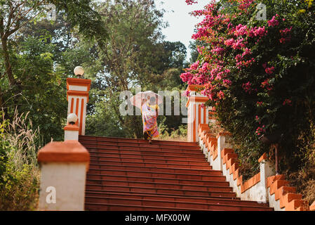 Indische Frau mit Regenschirm am Roten Hindu Tempel auf einem Hügel mit Blick auf Goa, Indien Stockfoto