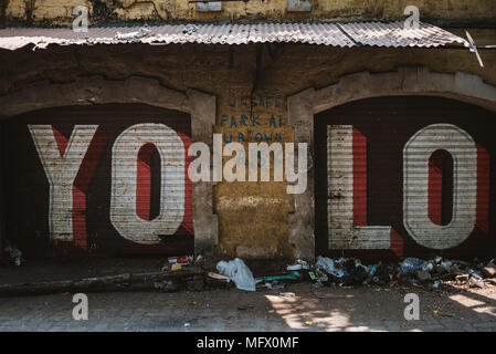 YOLO graffiti auf Garagentoren mit Papierkorb in Goa, Indien Stockfoto