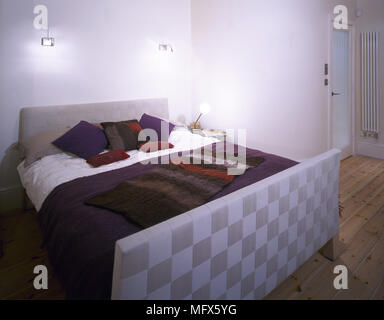 Modernes Schlafzimmer mit Holzboden, Glastür, Doppelbett mit einem gepolsterten Kopfteil und Fußteil und lila Bettwäsche. Stockfoto