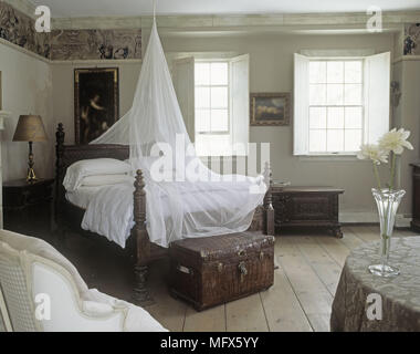 Ein Schlafzimmer mit Doppelbett mit weißem Tüll Fenster mit Fensterläden und Holzböden. Stockfoto