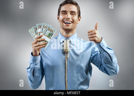 Mann mit Geld und zeigen den Daumen nach oben. Fotos von lächelnden Mann im blauen Hemd und Krawatte in Form von Schleife am Hals auf grauem Hintergrund Stockfoto