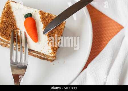 Hausgemachter Karottenkuchen mit Karotte Dekorationen auf weissen Teller, Gabel, Messer, Serviette, Ansicht von oben. Stockfoto